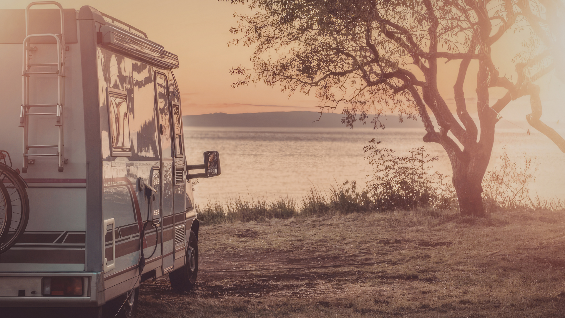 Camping-car stationné au bord d’un lac au soleil couchant